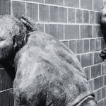 Bronze statues listening to the secrets within a brick wall