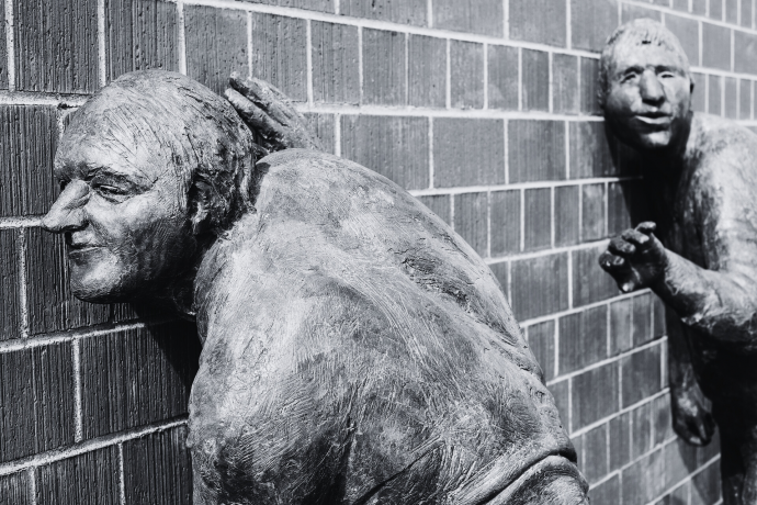 Bronze statues listening to the secrets within a brick wall