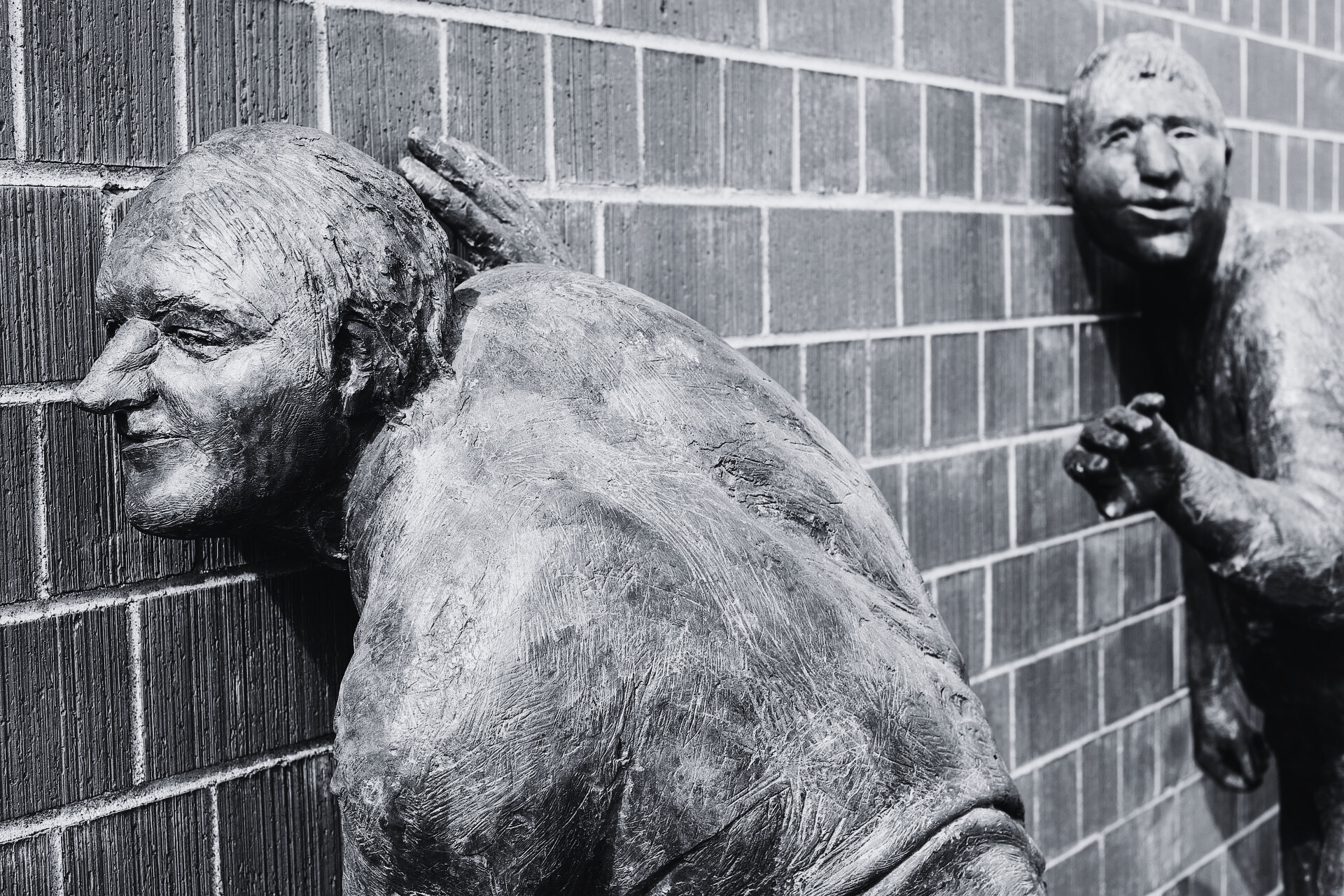 Bronze statues listening to the secrets within a brick wall