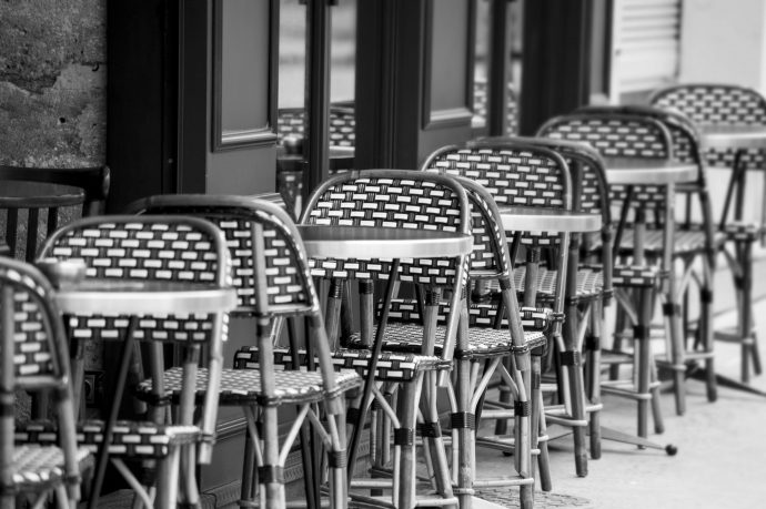 A line of wicker patio chairs and glass bistro tables on a streetside patio.